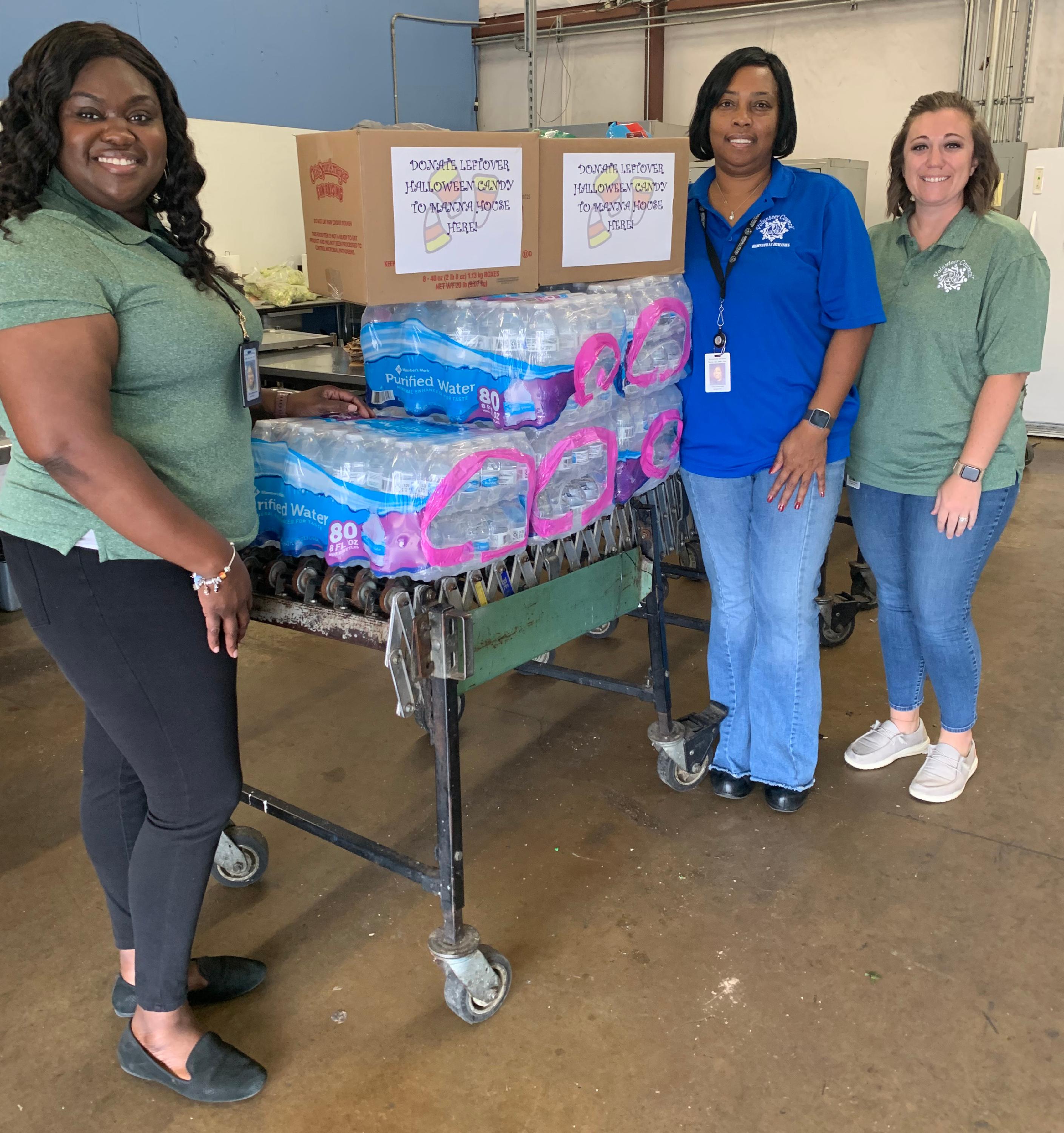 Three people standing next to a table to donated food and water. 